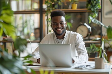 Portrait of smiling male IT professional sitting at desk with laptop and taking notes in modern office, copy space for text banner stock photo concept. Smiling young man working on computer using