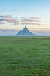 Silhouette of Mont Saint Michel cathedral on the island with green meadow at sunrise, Normandy, France. Tidal island with medieval gothic cathedral in Normandie. Vertical orientation