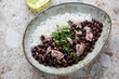 Oval bowl with cuban-style black beans and rice, horizontal shot on a light-brown granite background, elevated view