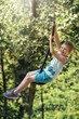 A little boy flying in the air with a breeze on a rope swing like Tarzan. Sunny forest foliage background for happy summer vacation