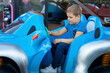 Happy smiling boy in blue clothes driving blue car toy at an amusement park