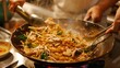 A chef skillfully tossing a sizzling wok full of Pad See Ew, with wide rice noodles, tender chicken, and crisp vegetables.