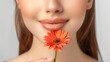 Closeup portrait of beautiful woman with perfect skin and natural make-up holding flower, half of face of attractive model. Indoor studio shot isolated over gray background.