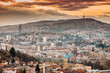panorama of Sarajevo as the sun sets behind its rolling hills, casting a colorful hue over the cityscape.