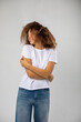 T-shirt design and advertising concept. Style and fashion. Indoor shot of cheerful smiling young African American woman with curly hair pointing index finger at copy space on her blank white top