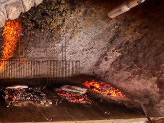 Grilling fish in a coastal restaurant at the Gargano Coast, Apulia, Italy, Europe. Brick wall with a fireplace in the center.  Several fish are cooking over the fire. Atmosphere is warm and cozy