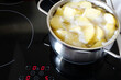 Peeled potatoes boiling in small metal pan on the modern induction stove in the kitchen
