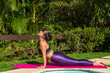 © Madu Oliveira - Mulher pratica yoga e se alongando ao ar livre e ao fundo veetação do jardim
