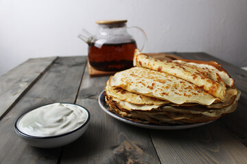 Canvas Print - The crepe pancake is stacked on a plate with sour cream and a cup of tea. Russian Breakfast