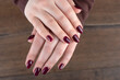 Female hands with trendy blackberry color manicure on nails over wooden background.