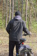 one man in a black jacket stands with his back and holds a bicycle on the street in nature