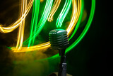 Fototapeta Kuchnia - Microphone for sound, music, karaoke in audio studio or stage. Mic technology. Speech broadcast equipment. Microphone in dark room on table with backlight. Selective focus