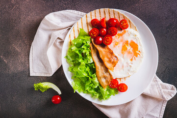 Poster - Close up of tacos with fried egg, bacon, tomato and lettuce on a plate on the table top view