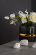 white flowers in a black vase, surrounded by stones on a gray background