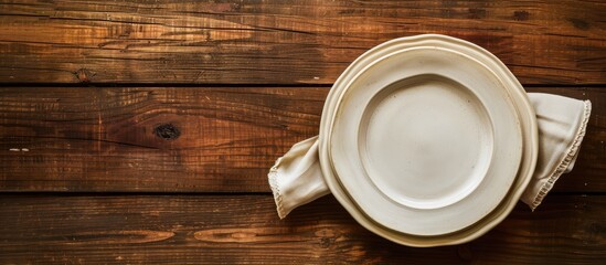 Wall Mural - An image showing a clean plate and a folded napkin on a brown wooden surface, with empty space for text. Viewed from above.