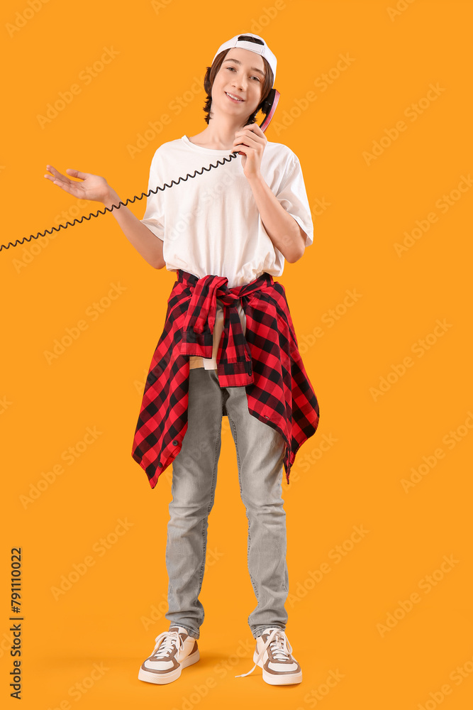 Cool teenage boy talking by telephone on yellow background