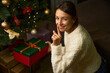 Smiling woman putting gift box under christmas tree and showing silence gesture