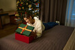 Young woman opening and looking inside gift box on bed during Christmas