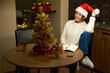 Woman wearing santa hat sitting at table and looking at camera during Christmas