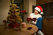 Young thoughtful and smiling woman writing her notes and wishes during Christmas