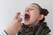 A little girl is sprayed with medicine in her mouth. A girl with a sore throat in a scarf with her mouth open. Selected focus.