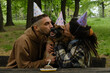 Dog celebrates birthday with family. Young couple hugs German Shepherd from both sides in spring green park. Dog birthday party with meat cake and 7 candle, paper hats on heads.