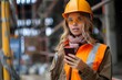 © Pinklife - A female construction worker with a hard hat and reflective vest looking at her phone on a worksite