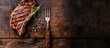 A fork holding a grilled ribeye steak on a weathered table, seen from above, with space available for your text.