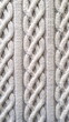 A detailed close-up showing the intricate patterns of a cream-colored cable knit fabric, highlighting the intertwined yarn - Generative AI