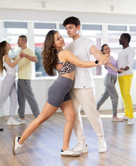 Poster - Smiling young couple, graceful girl and expressive Hispanic guy in sportswear enjoying slow foxtrot in dance studio. Amateur ballroom dancing concept