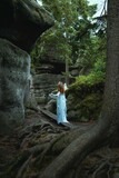 Fototapeta Londyn - a woman in a fairy blue dress with a flower on her head stands in front of a rock wall.