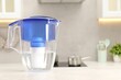Water filter jug on light grey table in kitchen, space for text