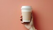 Hand holding a white paper cup with a black lid On a yellow background there is space for text or advertisements. Suitable for promotion