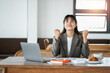 © Satori Studio - Businesswoman in office attire celebrates a success with a fist pump in front of her laptop at her desk.