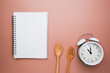 Intermittent fasting background includes clock, spoon, fork and notebook for diet plan.