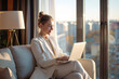 © 수동 김 - A woman in casual business attire sitting on the sofa of her modern apartment, working from home on her laptop and smiling at the camera