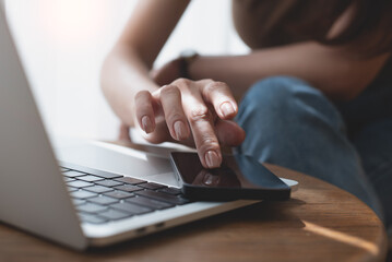 Poster - Close up of woman hand using mobile phone, finger touching on screen, searching the information during working on laptop computer on table at home office