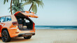 A orange SUV with its trunk open on a beach.