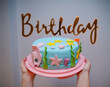 Closeup of woman hands holding beautiful birthday cake with words birthday in the back          