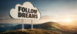 On a green grass sunrise hill is a cloud shaped sign board with the words 'follow dreams' - Visual metaphor for never giving up, always endure, pursue your goals.