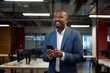 Mature black man in businesswear smiling while using mobile phone in office