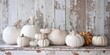White pumpkins and gourds of various sizes sit on a rustic wooden table against a peeling whitewashed fence creating a simple, yet, elegant still life.