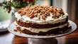 Close-up of a gluten-free carrot cake with cream cheese frosting, decorated with walnut pieces, on a cake stand. 