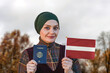Muslim Woman Holding Passport and Flag of Latvia
