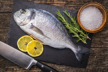 Wall Mural - Fresh sea bream fish on cutting board on wooden table. Top view.