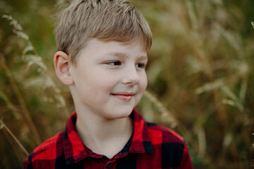 Poster - Portrait of young boy standing in nature, in the middle of tall grass, headshot. Copy space.