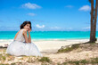 Young woman in white dress sitting on beach by ocean