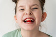 Little cheerful girl holding a red pill in her teeth. Selected Focus