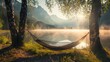 A serene summer camping scene at a lake, featuring an empty hammock between two trees with a view of a foggy mountain lake at sunrise. The scene promotes an outdoor and adventure theme
