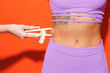 Close up cropped young fitness trainer instructor sporty woman sportsman in purple top clothes in home gym hold use caliper for waist isolated on plain orange background Workout sport fit abs concept.